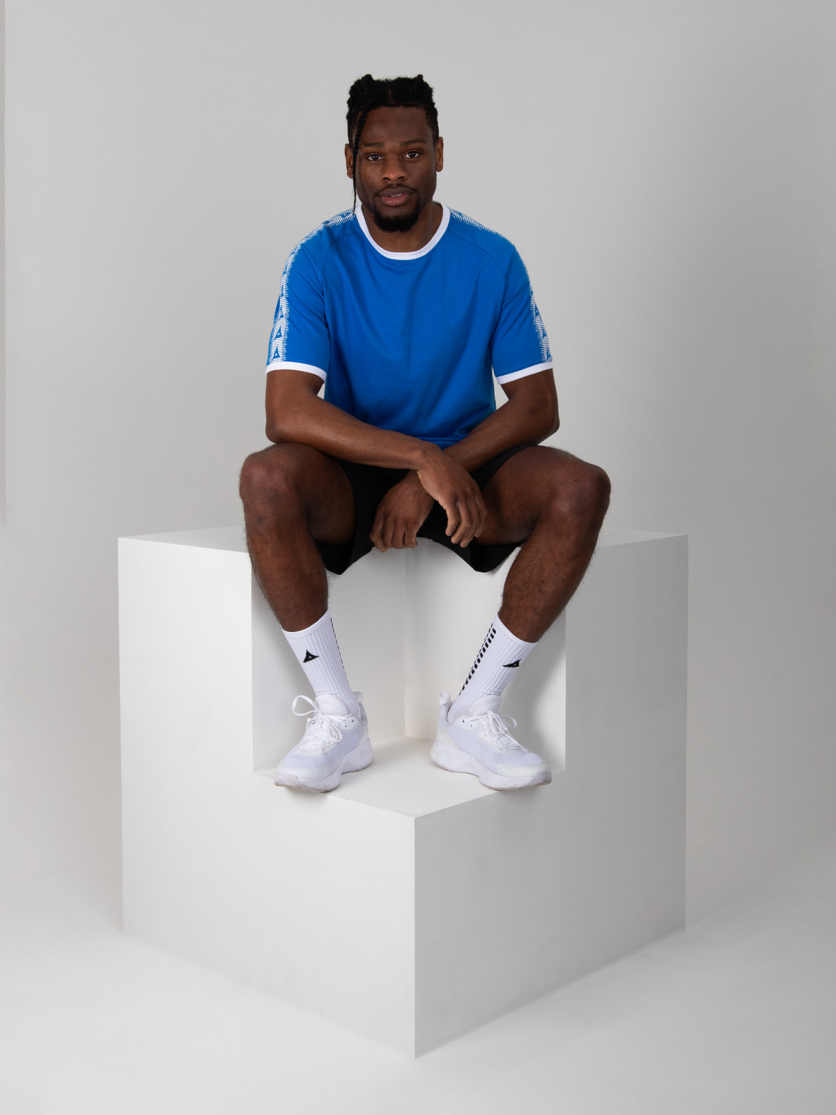 a model is sitting down on a cube wearing a royal blue cotton t-shirt with white trim details. 