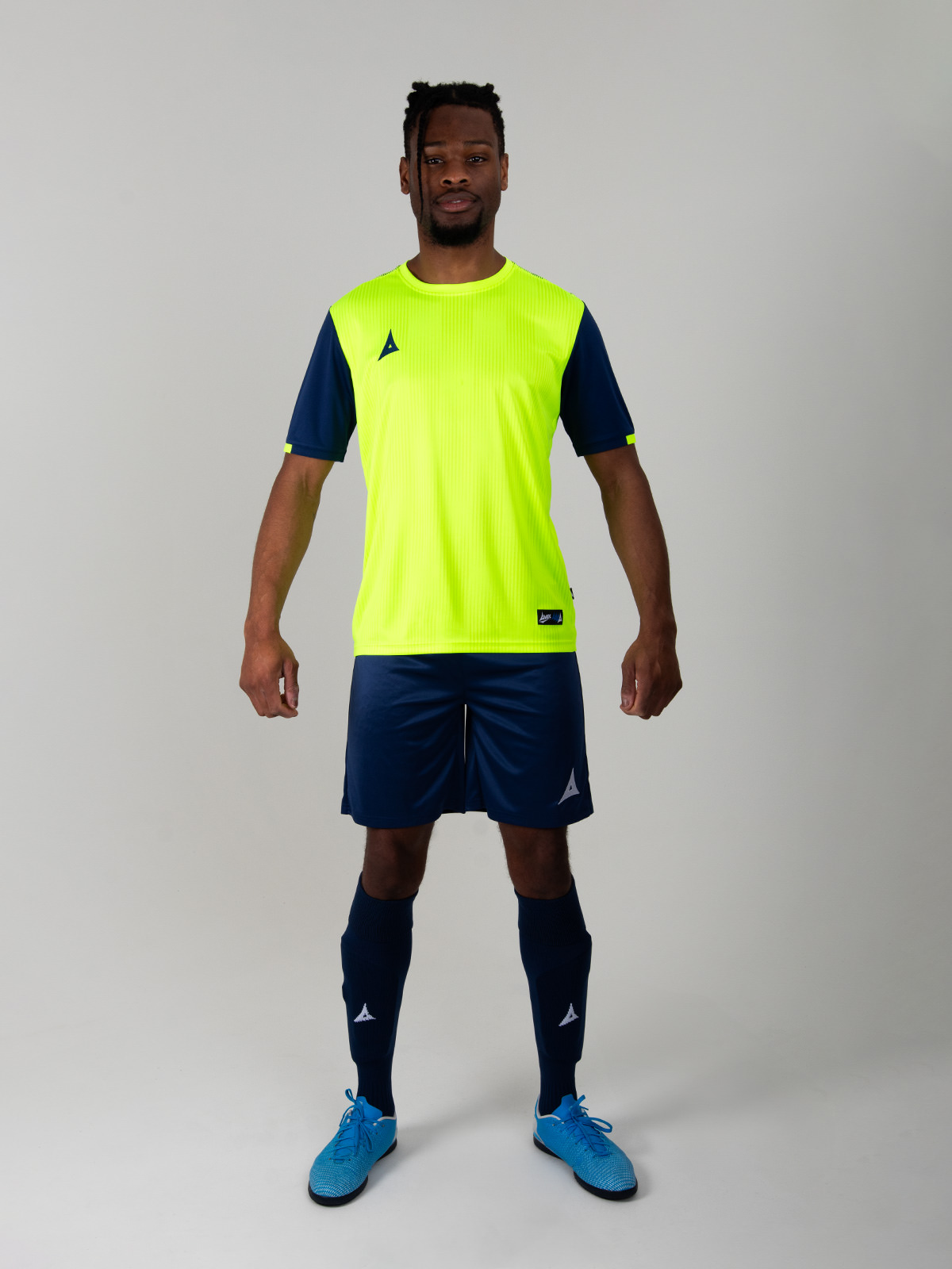 the model is wearing a bright yellow football shirt with navy sleeves, and the look is completed with navy shorts and navy socks. 