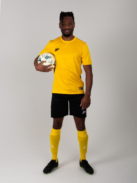 A man is wearing a yellow football kit, but has black shorts in this combination.