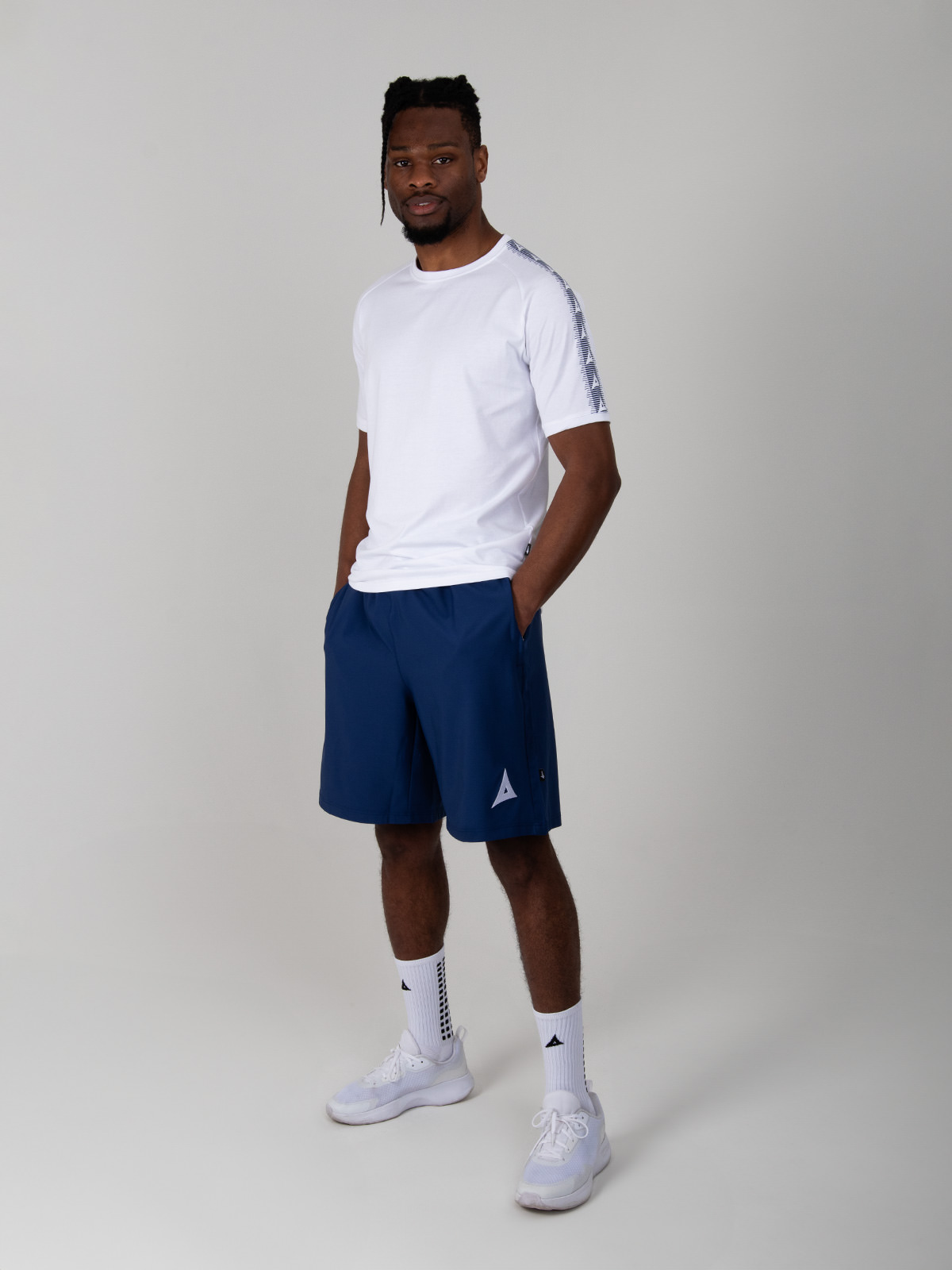 model standing up wearing a plain white cotton t-shirt with avec logo taping print on sleeves, navy blue coaching shorts and white grip socks