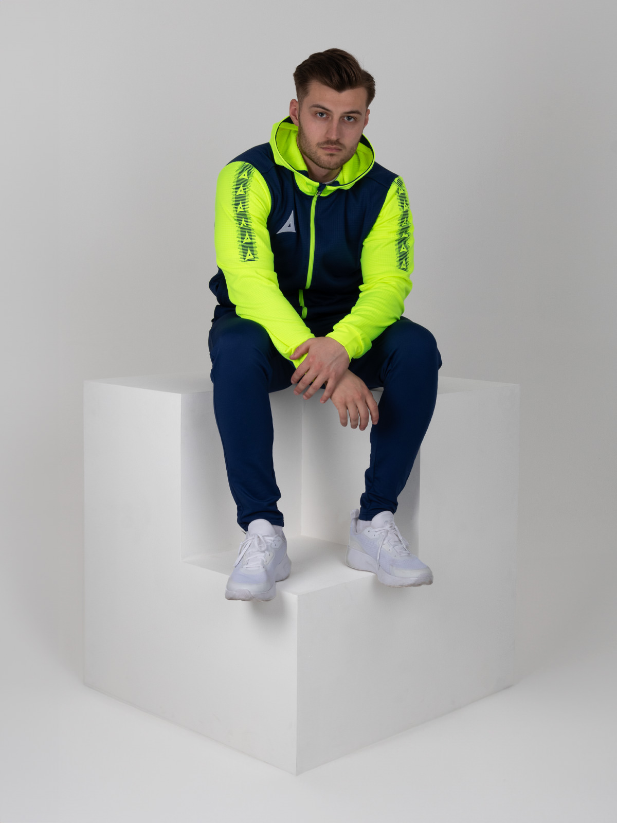 a man sitting on a cube wearing a bright navy and yellow full zip hoody