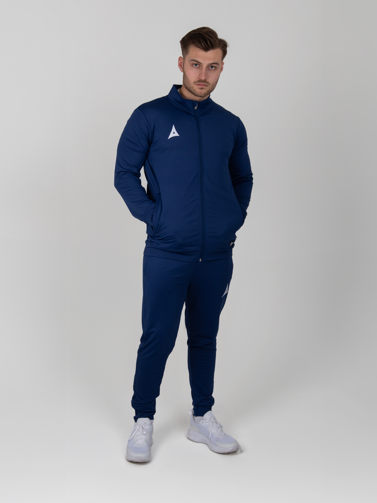 a man is wearing a fully zipped navy tracksuit jacket and matching navy jogging bottoms