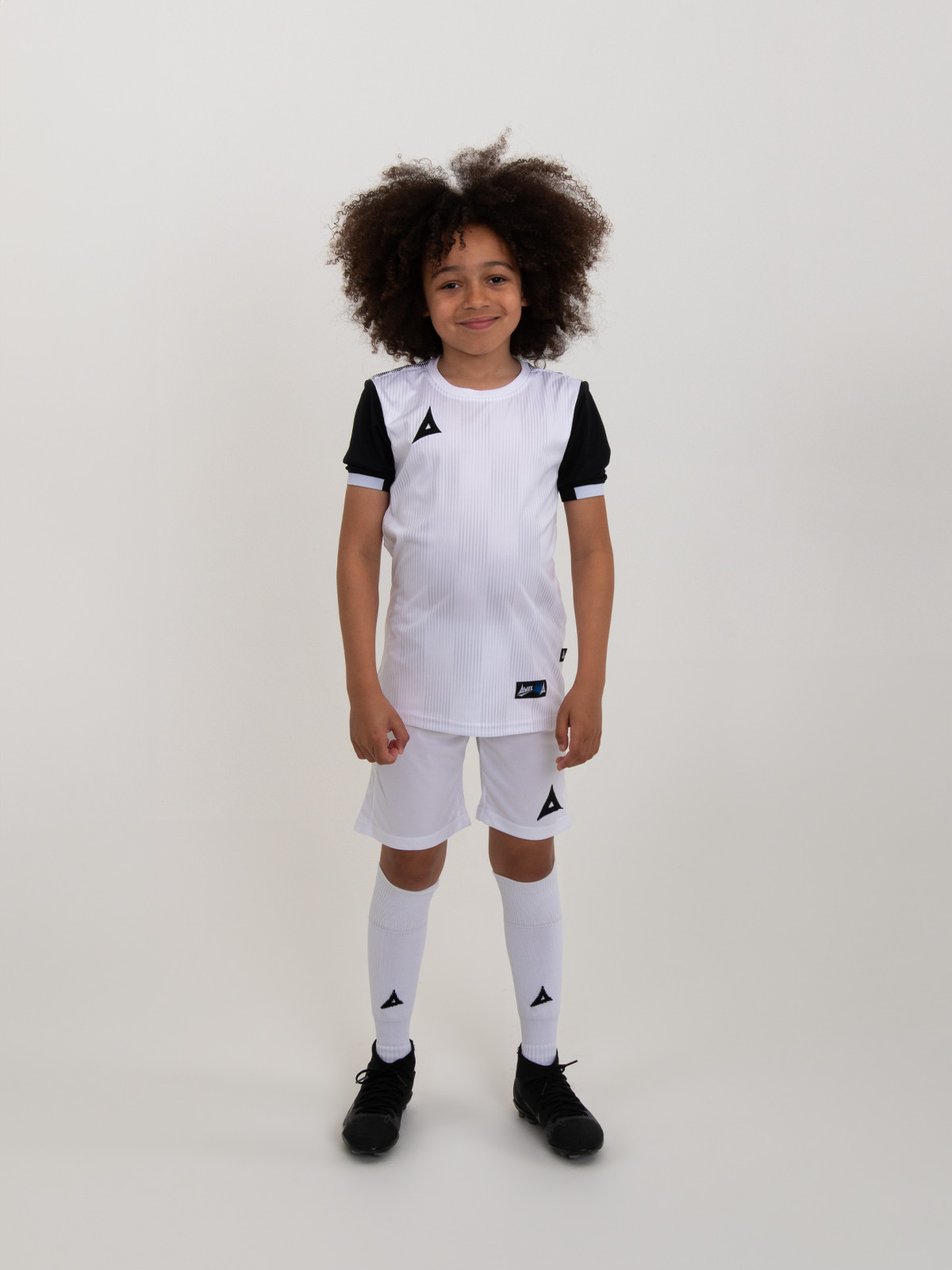a child is wearing a white football kit with black sleeves and trim. this combination is using white shirt, white shorts and white socks