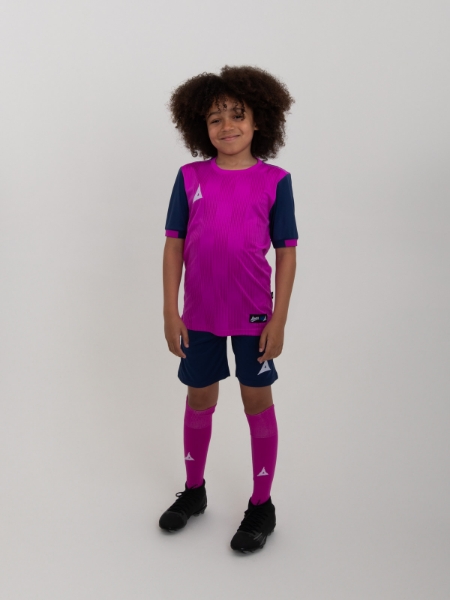 A kid is wearing a purple football shirt with navy shorts and socks. The shirt has a two-tone graphic print on it