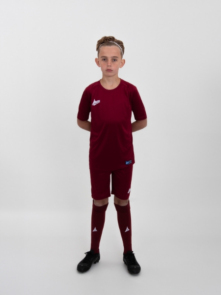 A child is wearing a full plain claret football kit