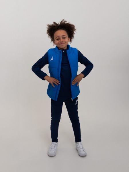 A kid is wearing an unzipped royal blue padded gilet over the top of a jumper to keep warm.