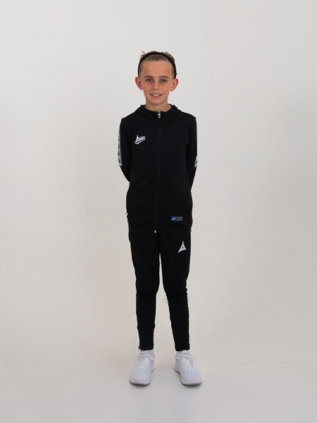 A boy has his hands behind his back while wearing a black hooded tracksuit