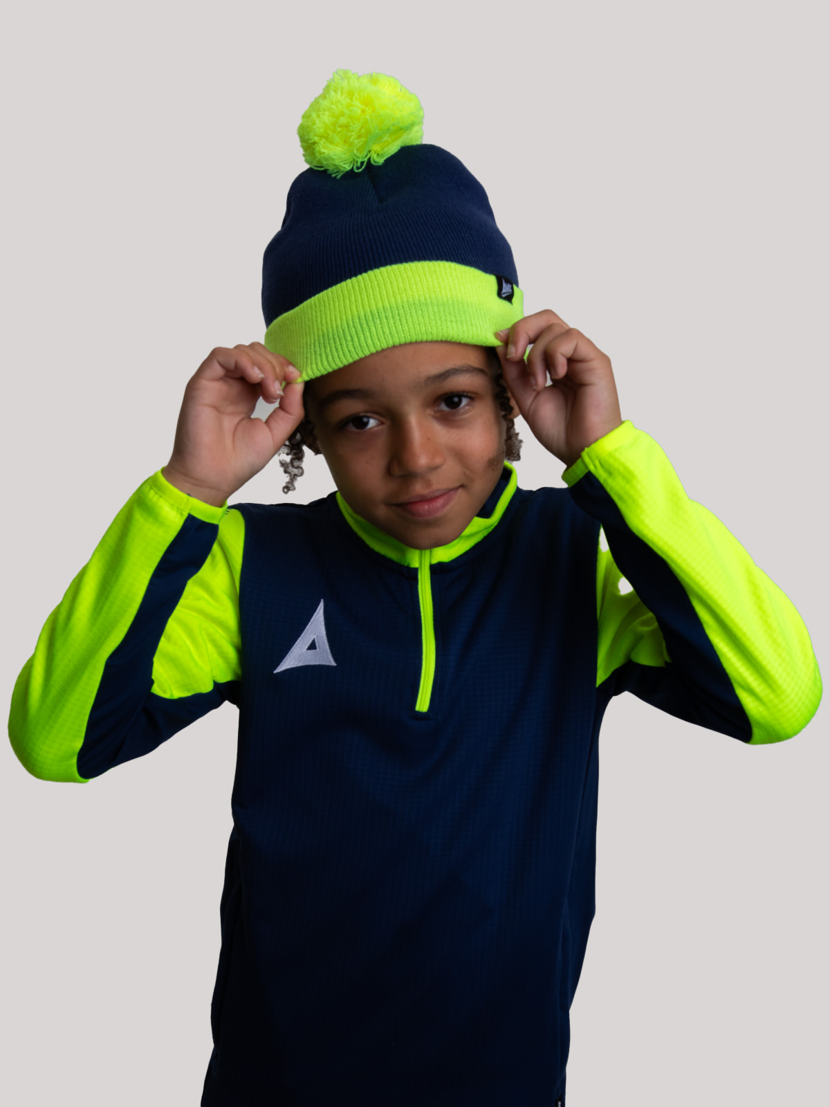 a child is wearing a navy kids bobble hat with a bright yellow trim. 