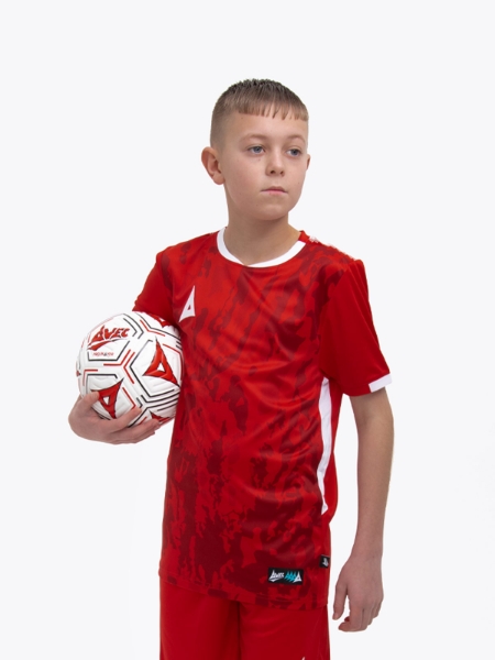 A young kid standing up wearing a red football shirt holding a red football