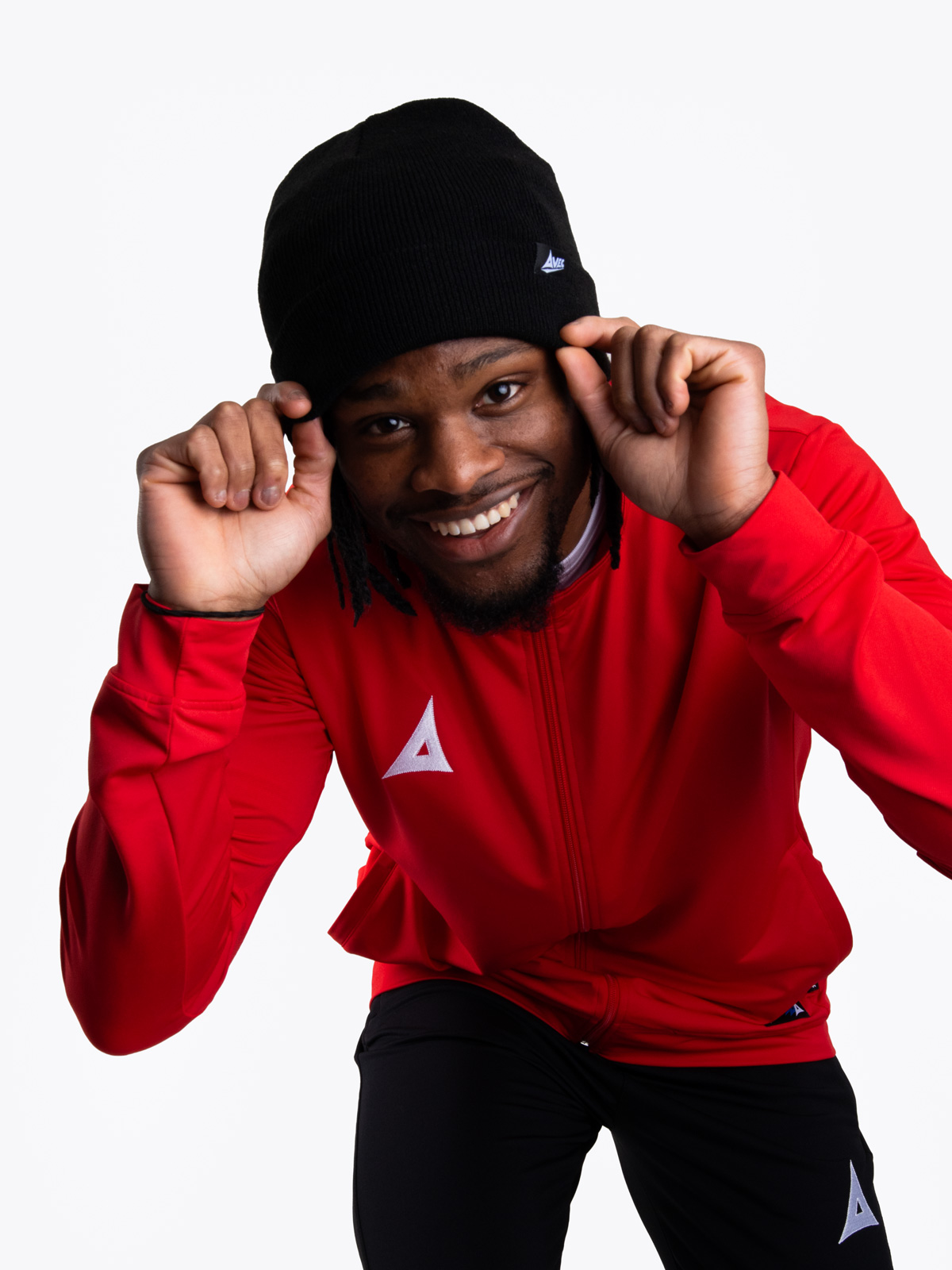 a man wearing a black beanie hat with a red track jacket on