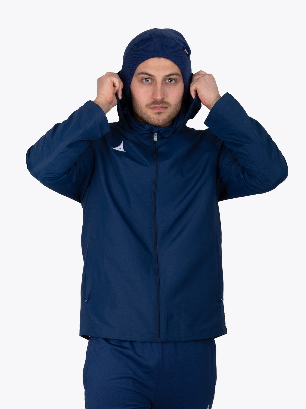 a man wearing a navy rain jacket and a matching navy turn up beanie putting his hood up