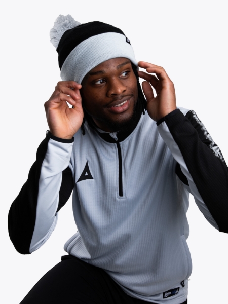 A man is wearing a grey bobble hat in black and grey.
