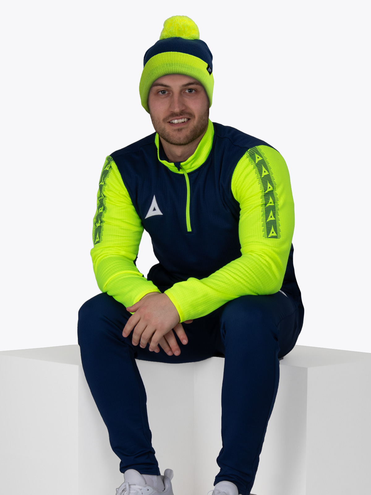 person in navy blue and neon yellow athletic outfit sitting on geometric block