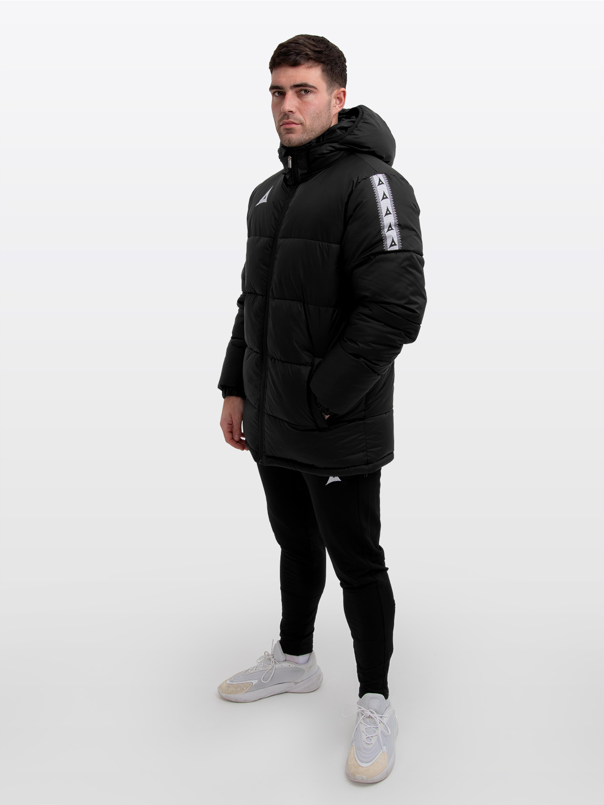 male model wearing the avec evolve pro padded jacket in black featuring avec heritage ‘a’ contrast sleeve logo design and medium padding for a refined, insulated fit. featuring avec black focus 2 track pants
