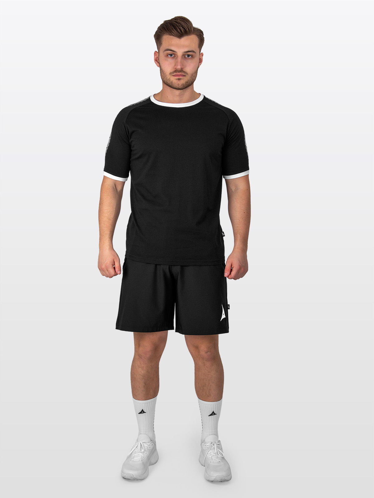 a male model is stood wearing the avec evolve black t-shirt, and black avec focus 2 tech shorts and white avec grip socks