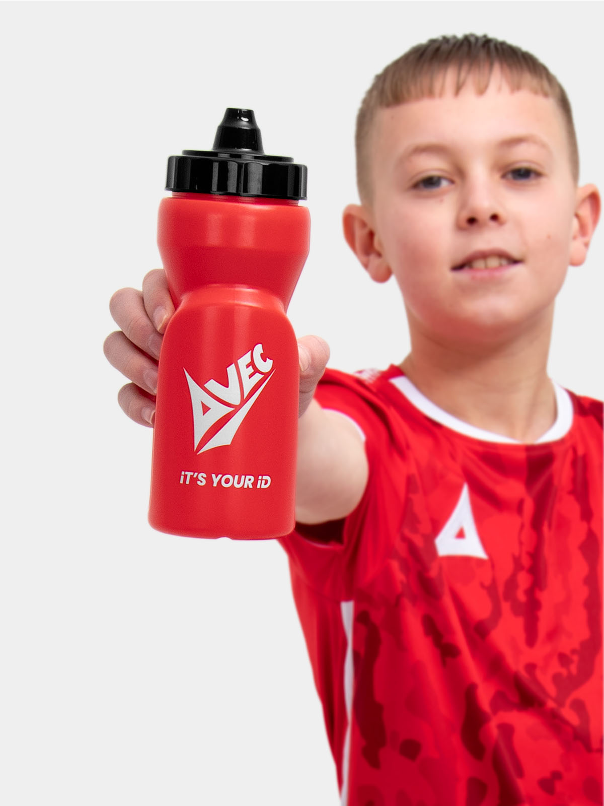 a kid is wearing a red football shirt with white panels and is drinking from a red water bottle with a self sealing nozzle