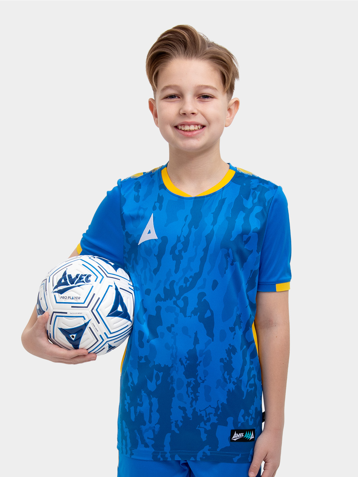 a kids football kit in royal blue and yellow with matching blue shorts and socks holding a football