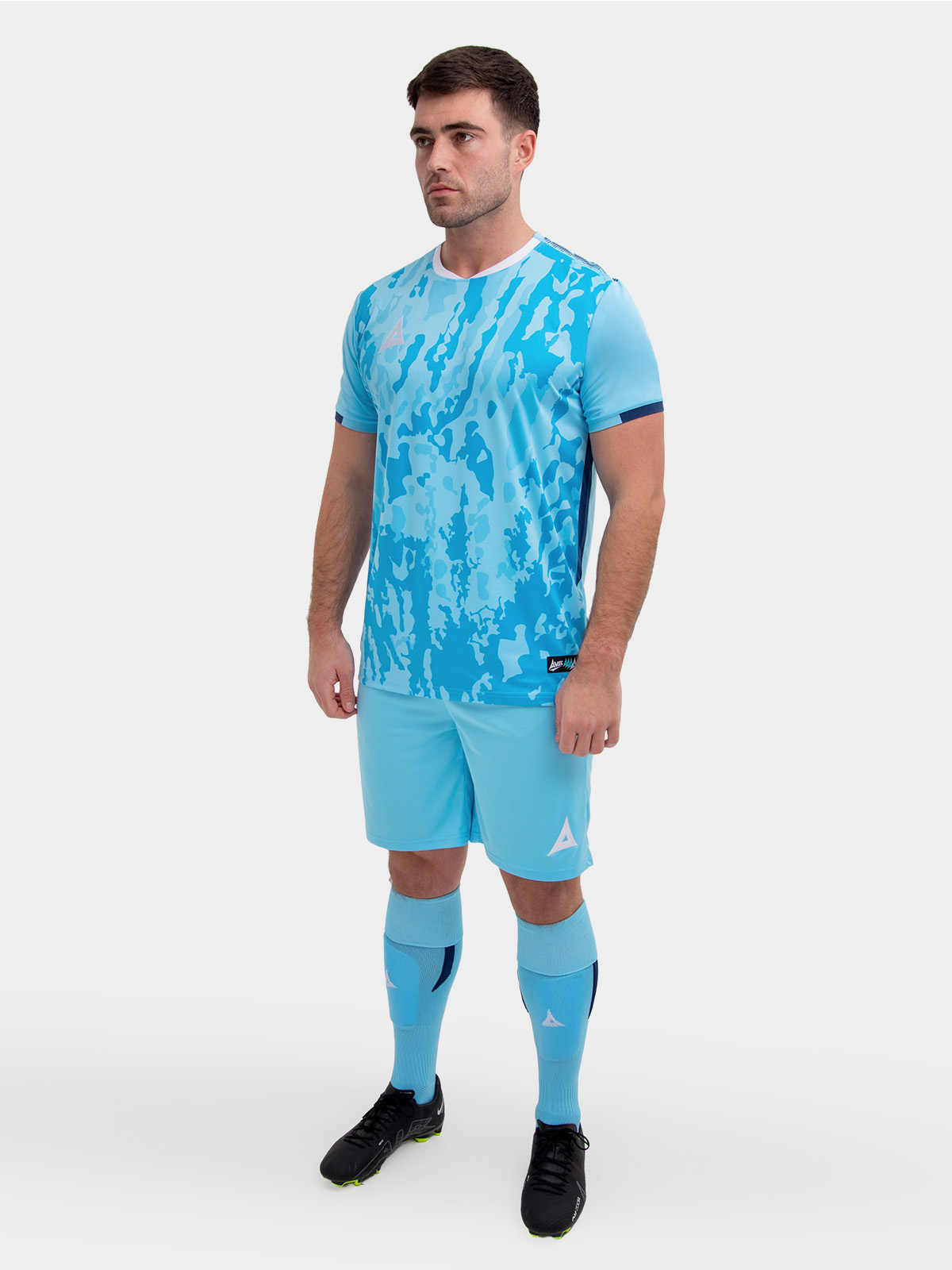 a model standing up wearing a sky and navy football shirt, sky shorts and sky football socks.