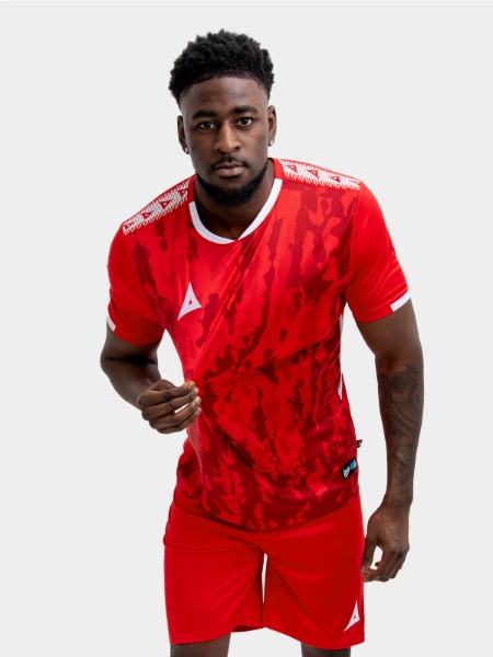 A man standing up wearing a red football shirt, matching red Shorts and red Football Socks.