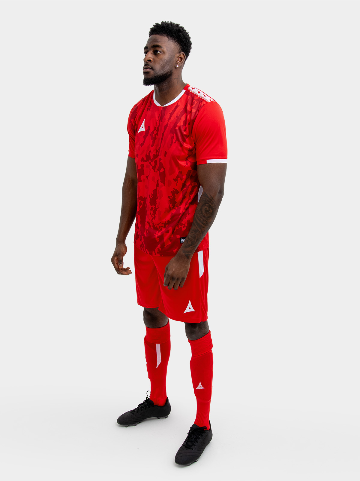 a man standing up wearing a red football shirt, matching red shorts and red football socks.