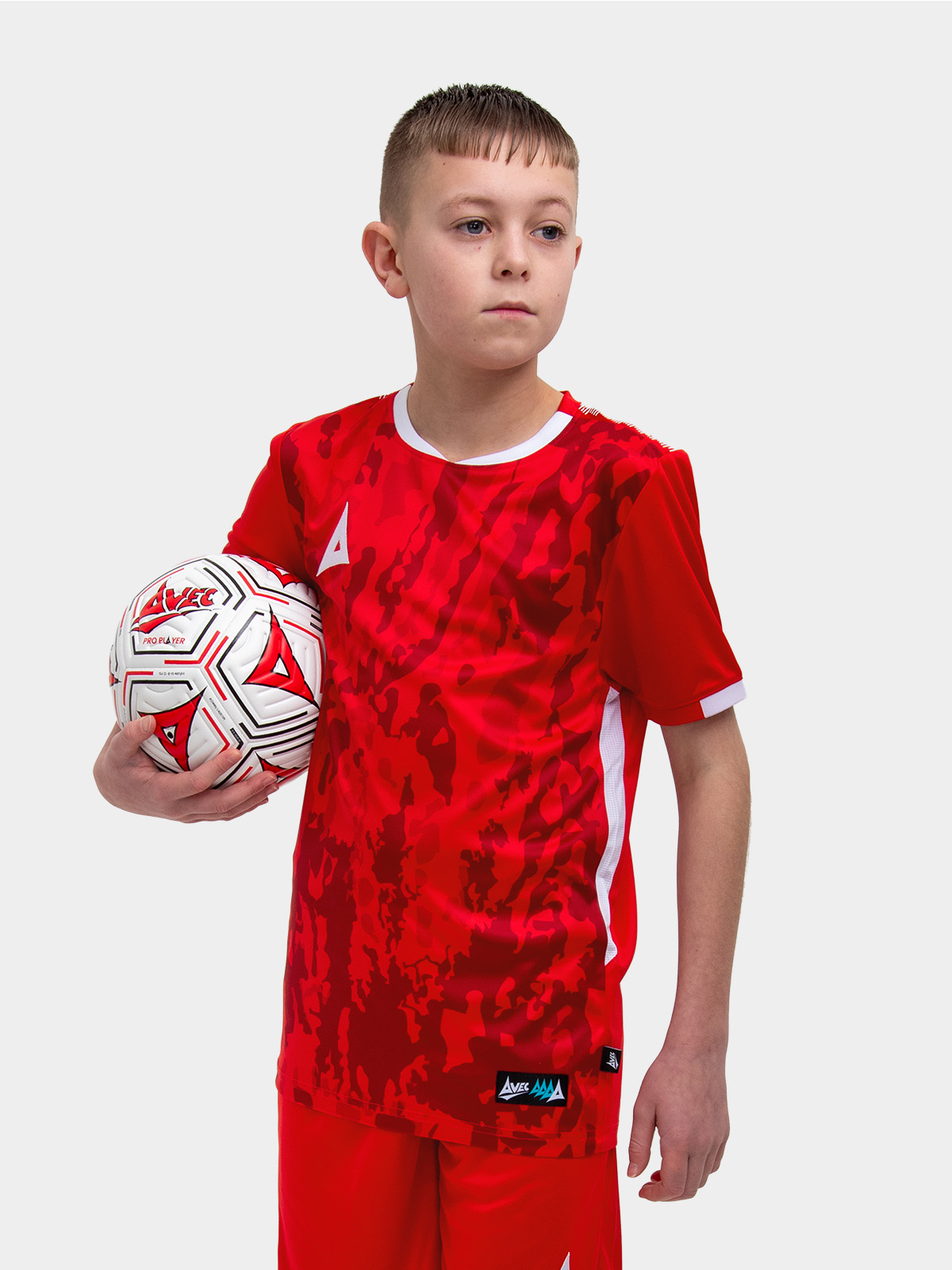 a young kid standing up wearing a red football shirt holding a red football