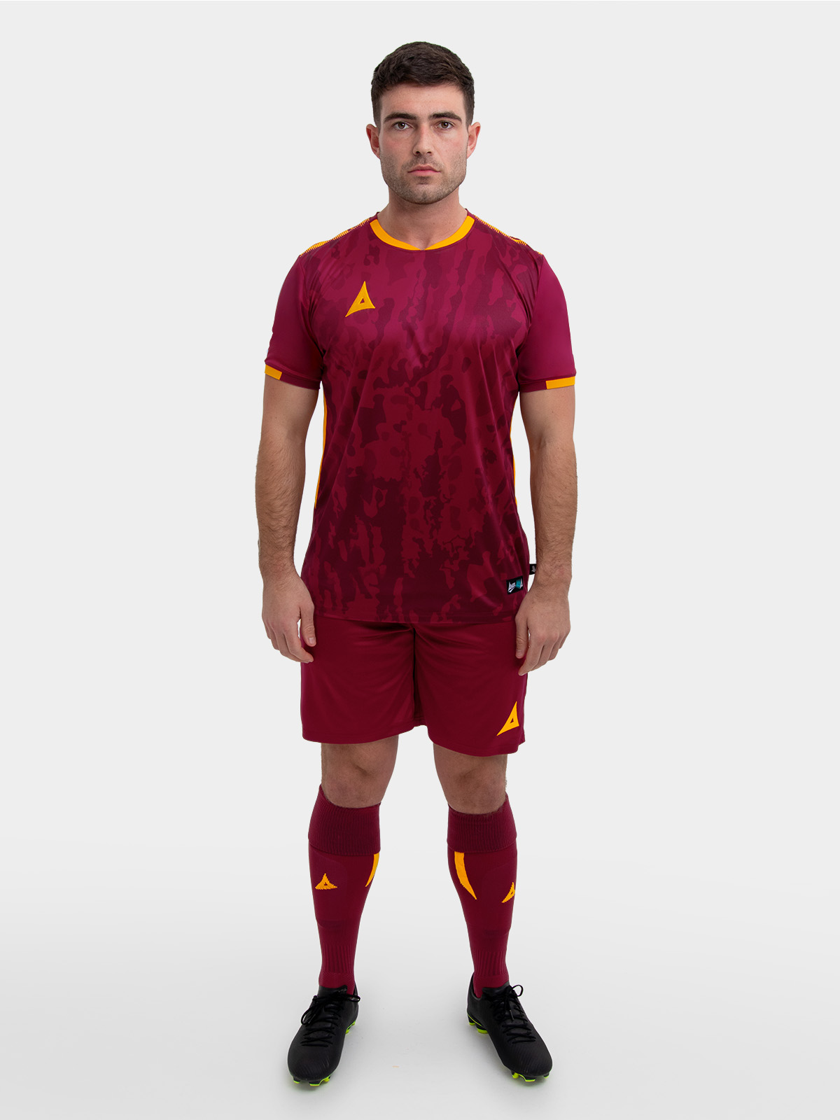 a model standing up wearing a claret / maroon football shirt, claret shorts and claret football socks.