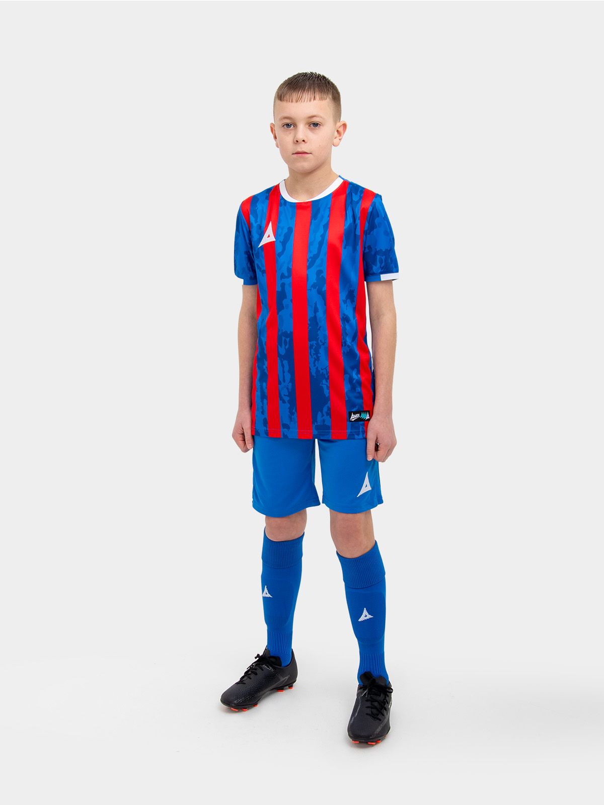 a kid standing up wearing a red and royal blue football shirt and matching socks and shorts