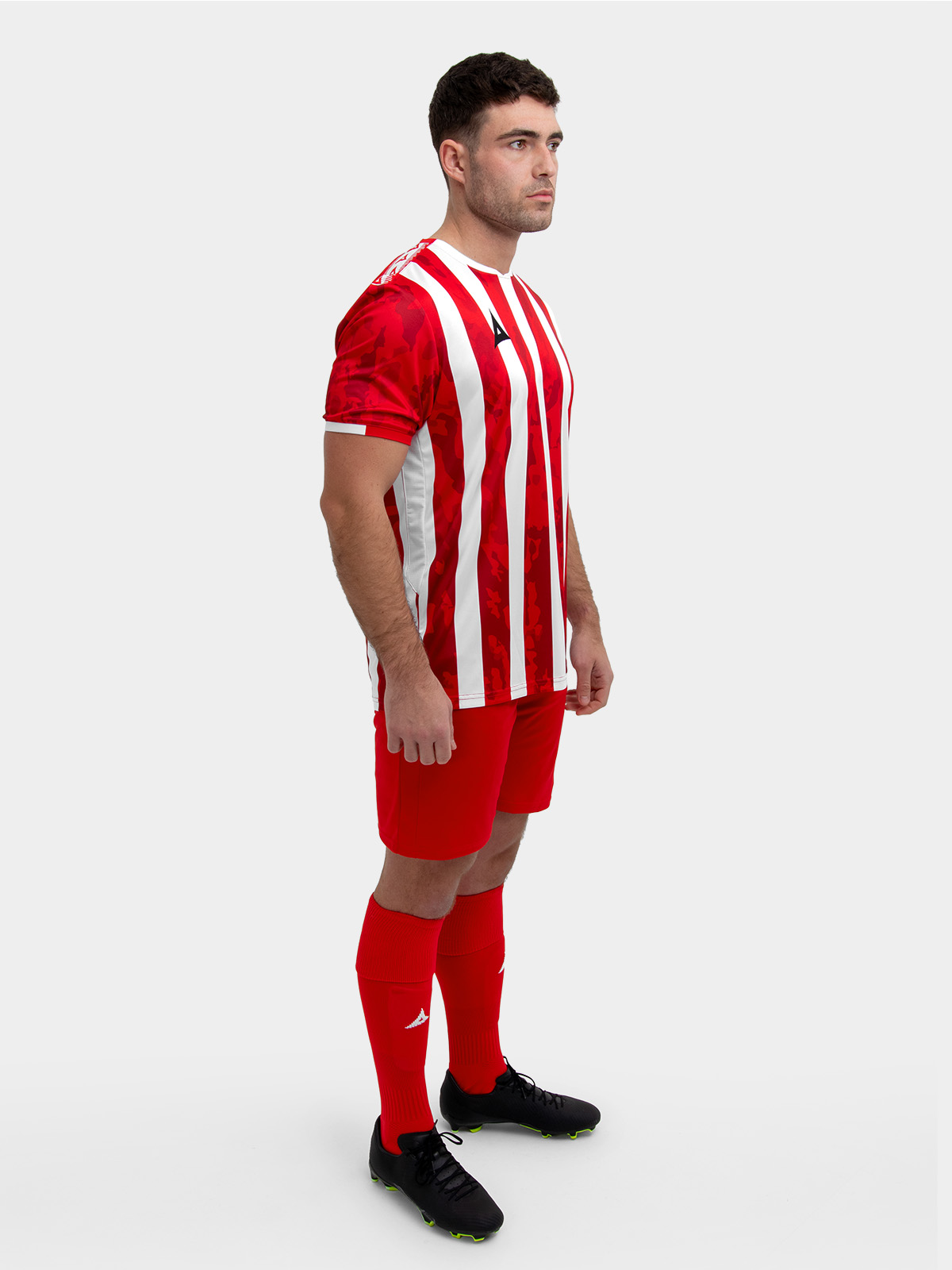 a model standing up wearing a red and white football shirt, red shorts and red football socks.