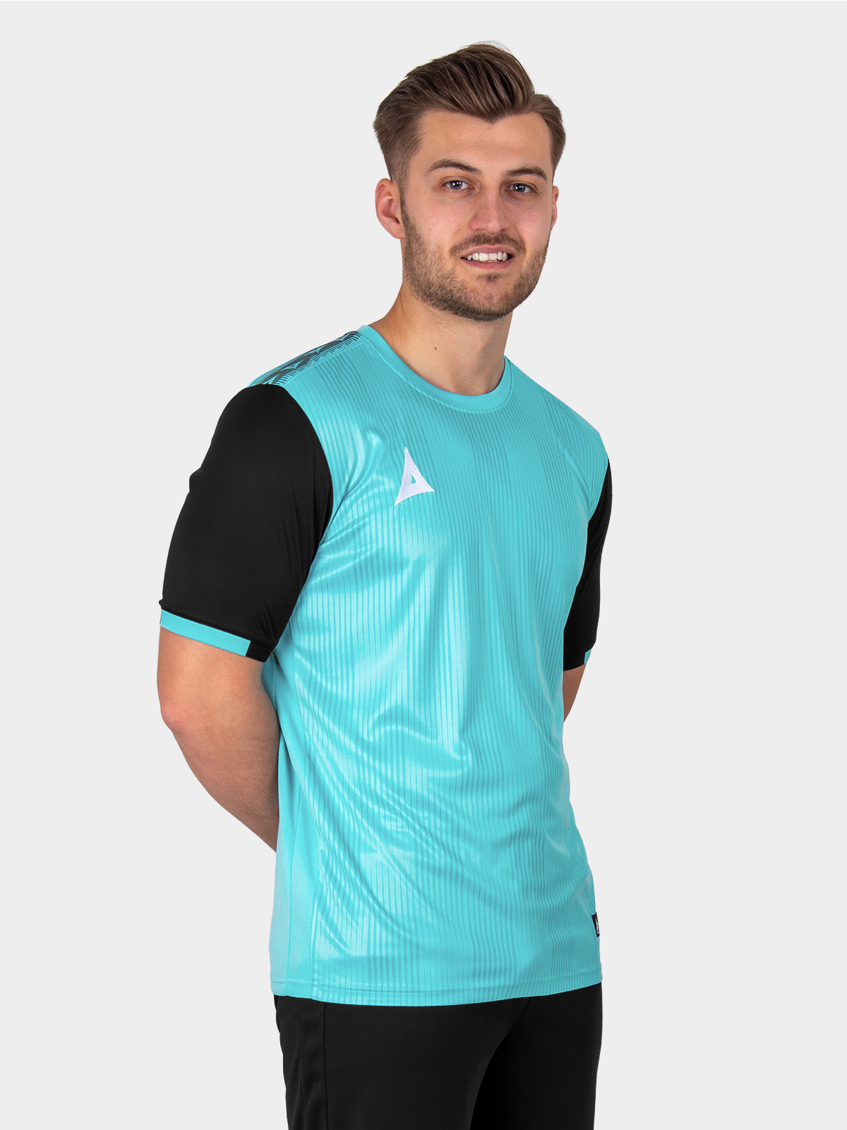 a model is sitting down posing in a light blue football shirt with black sleeves, black shorts and pale blue socks