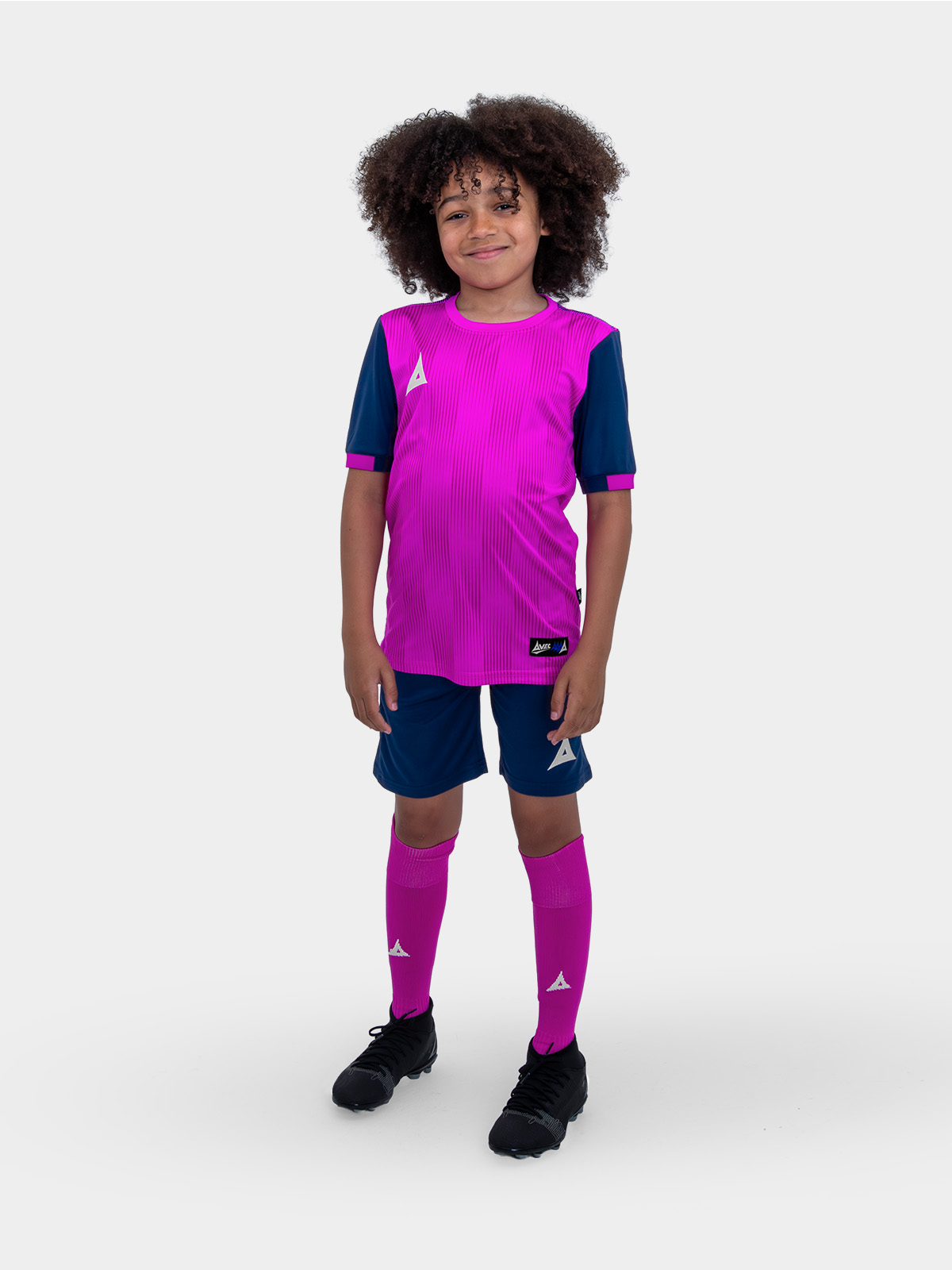a kid is wearing a pink football shirt with navy shorts and socks. the shirt has a two-tone graphic print on it