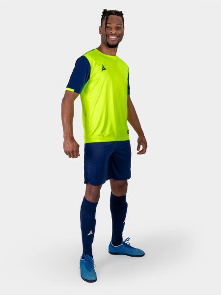 	The model is wearing a bright yellow football shirt with navy sleeves, and the look is completed with navy shorts and navy socks.