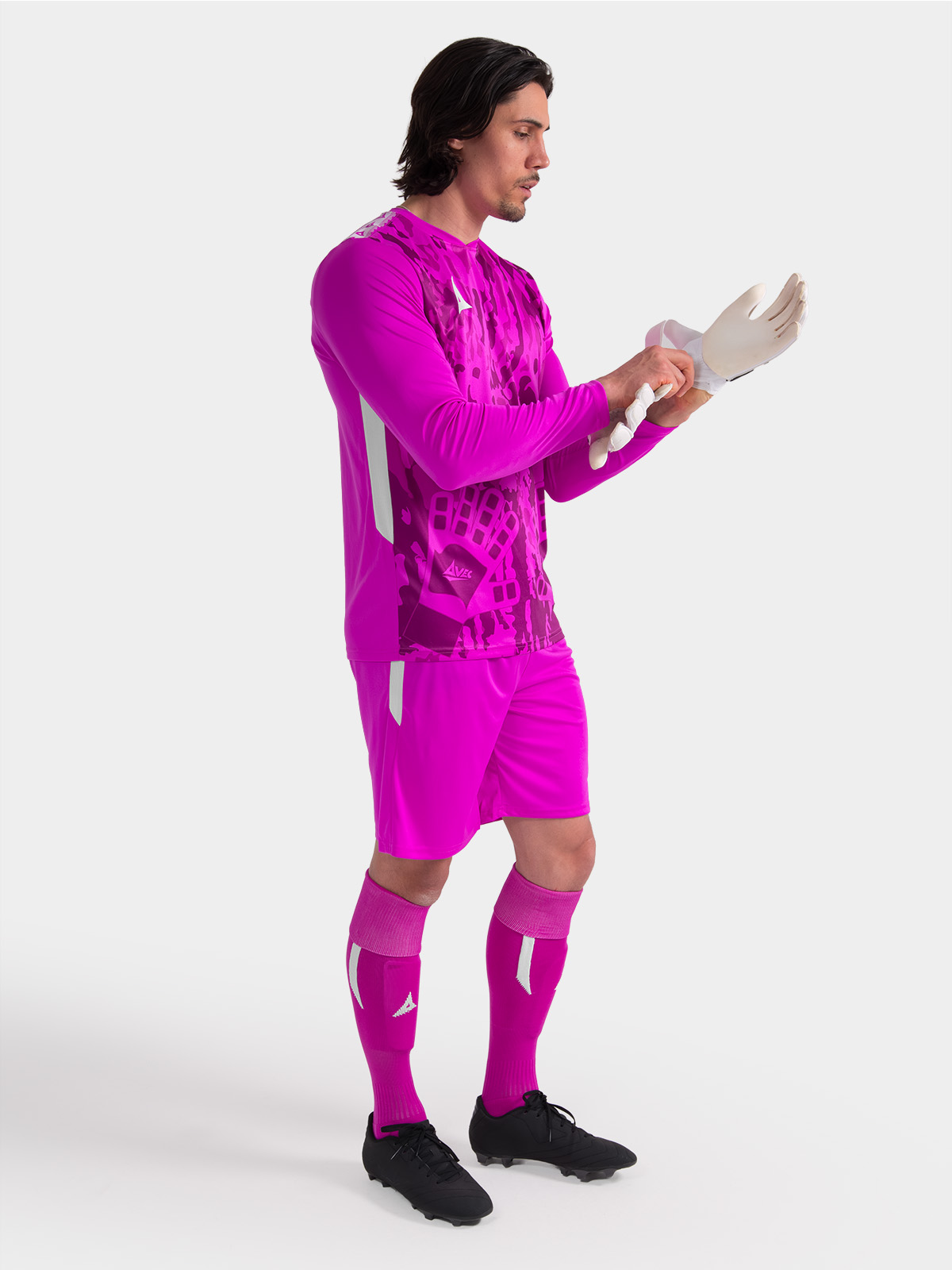 a model standing up wearing a magenta goalkeeper football shirt with a camo pattern and matching shorts and socks
