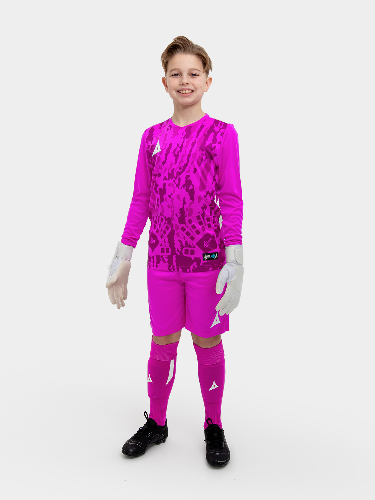 	a child standing up wearing a magenta goalkeeper football shirt and matching shorts and socks