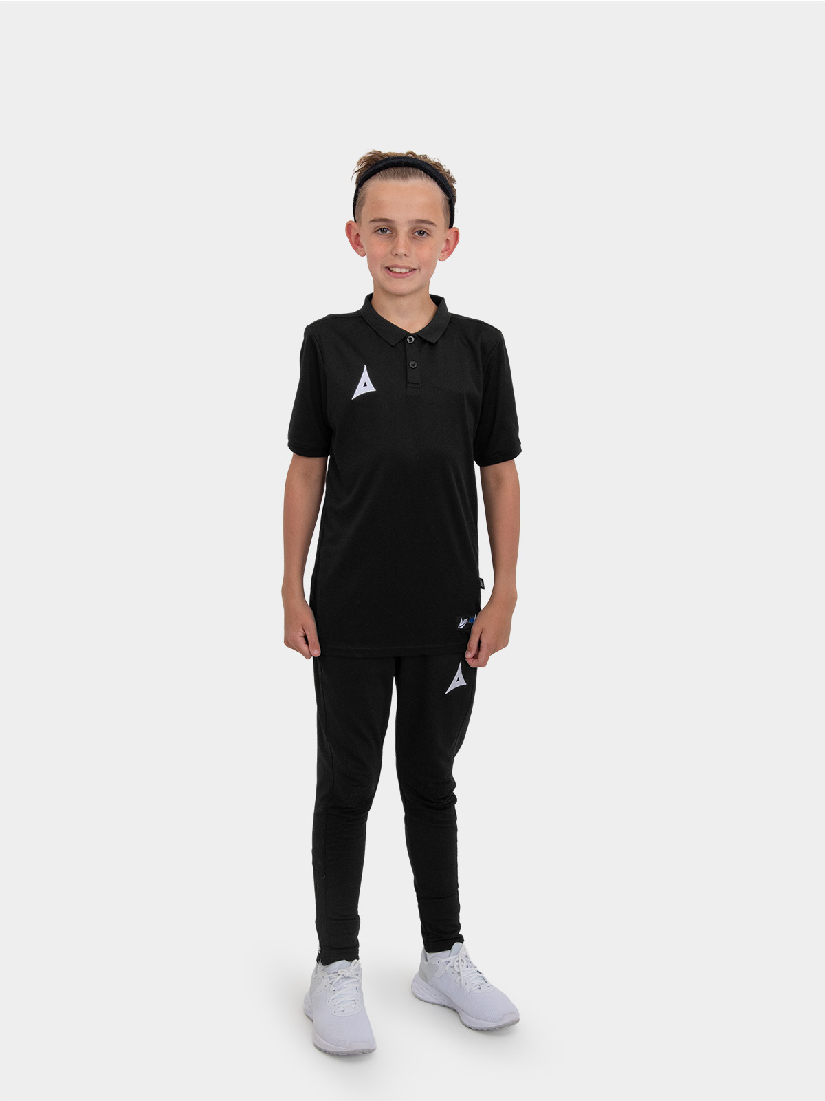 	a boy is stood wearing the avec focus 2 black tech polo and the avec focus 2 black tech pant ready for training