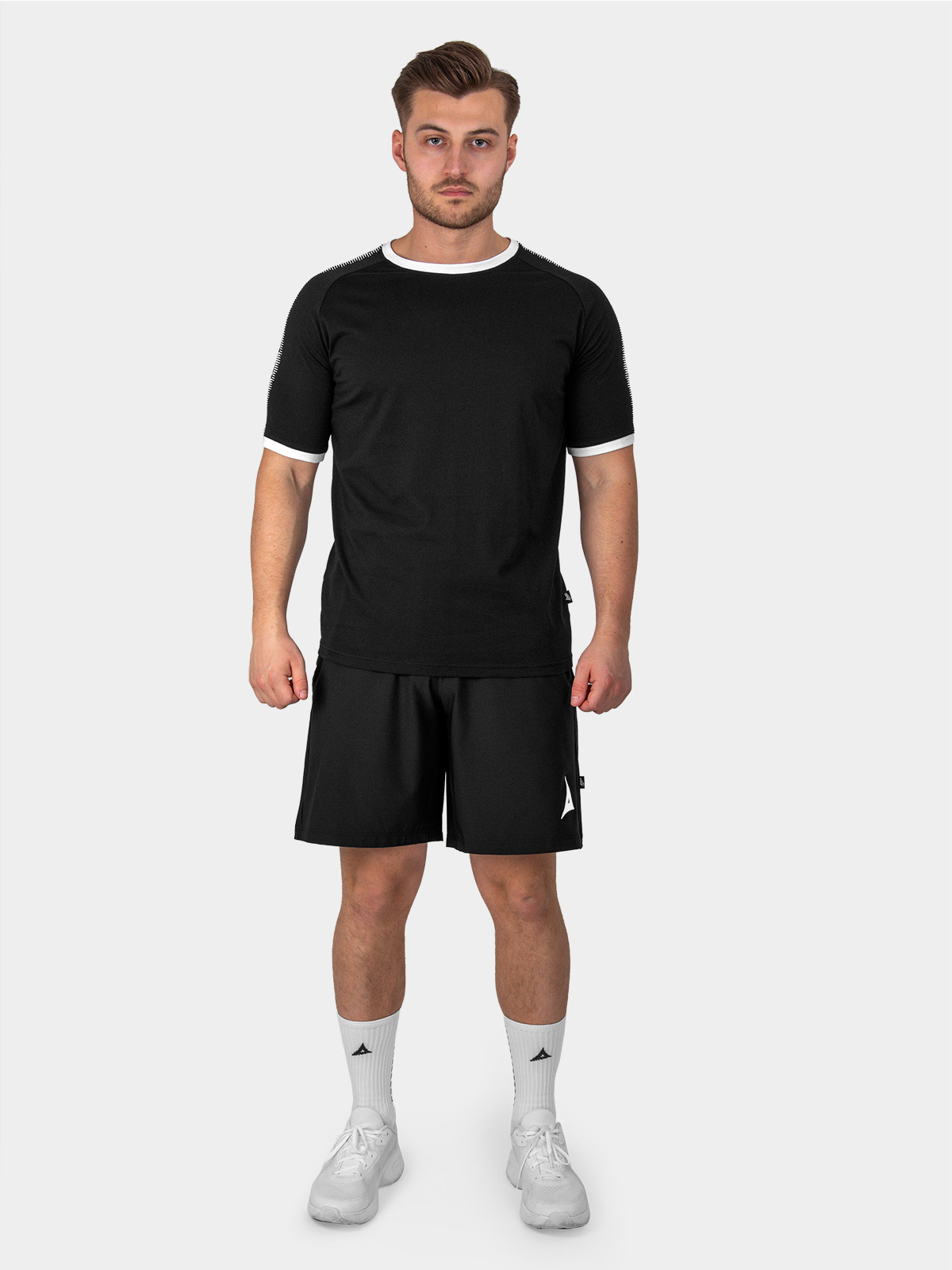 	a male model is stood wearing the avec evolve black t-shirt, and black avec focus 2 tech shorts and white avec grip socks