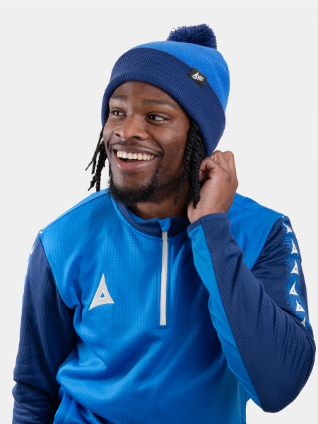 A man wearing a royal and navy blue bobble hat matching his overlay