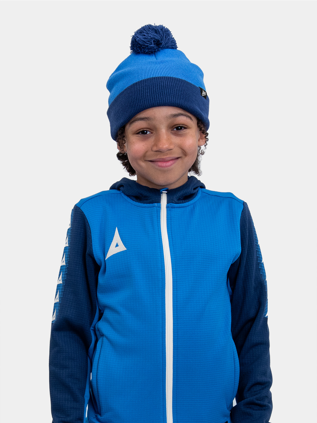 a young boy is wearing a royal and navy blue bobble hat matching his overlay