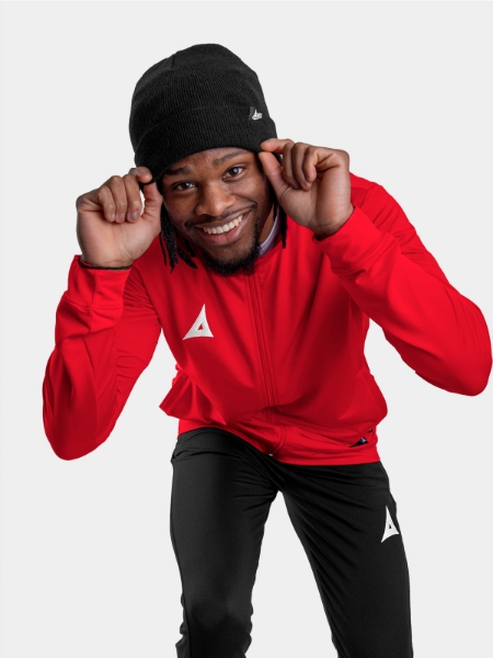 A Man wearing a black beanie hat with a red track jacket and black tech pants