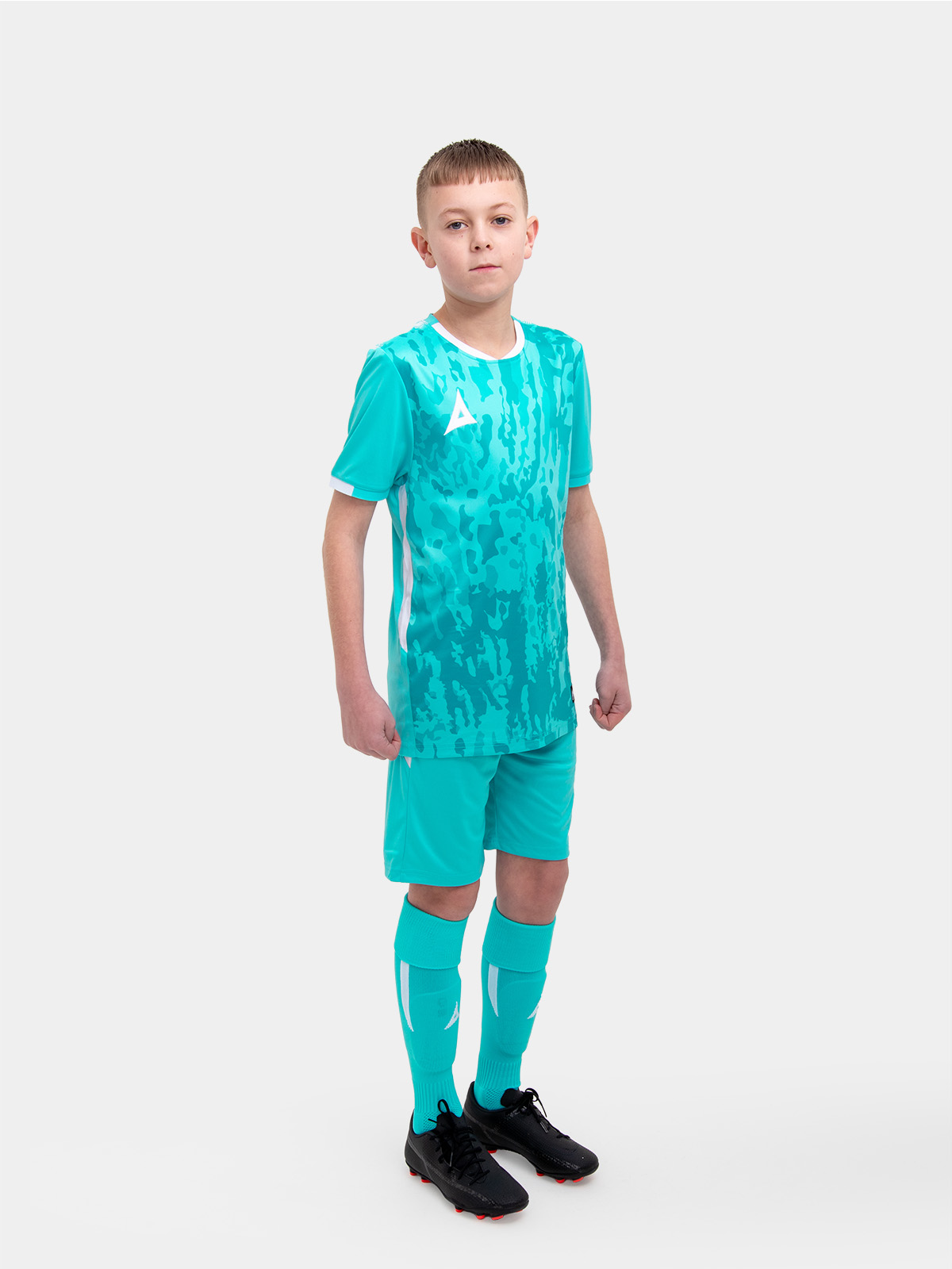 	a kid standing up wearing a hyper blue football shirt, matching hyper blue shorts and football socks.