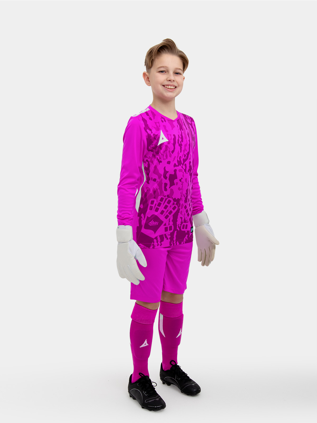 	a kid standing up wearing a magenta goalkeeper football shirt, magenta shorts and magenta football socks.
