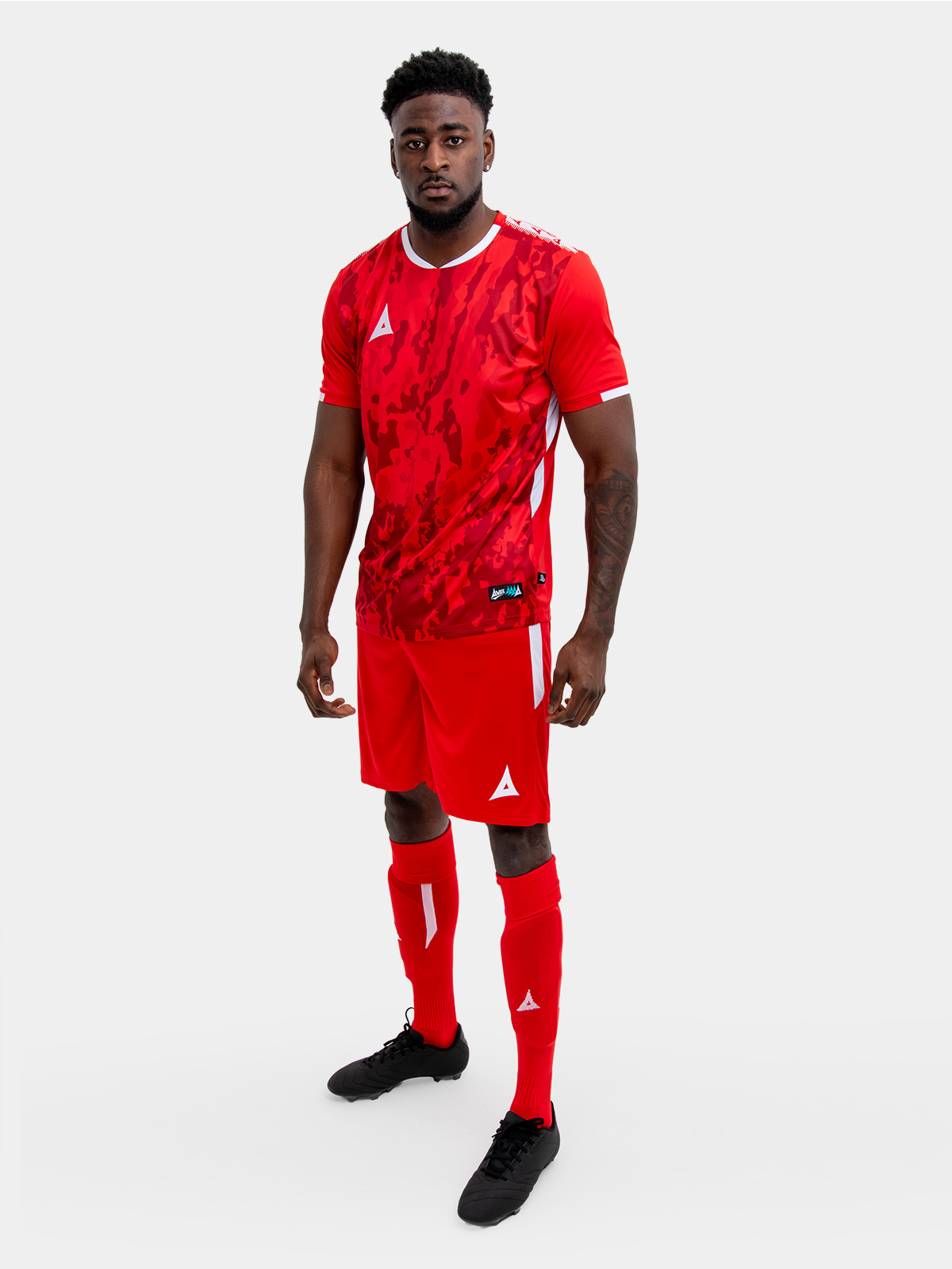 	a model standing up wearing a red football shirt, matching red shorts and red football socks.