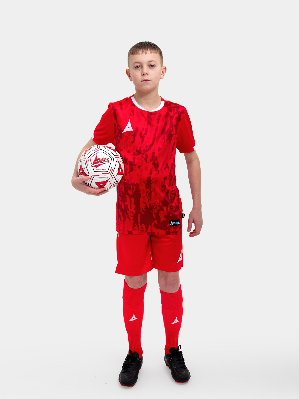 a young child is wearing a red football shirt. the football shirt has a camo pattern and matching red socks and shorts
