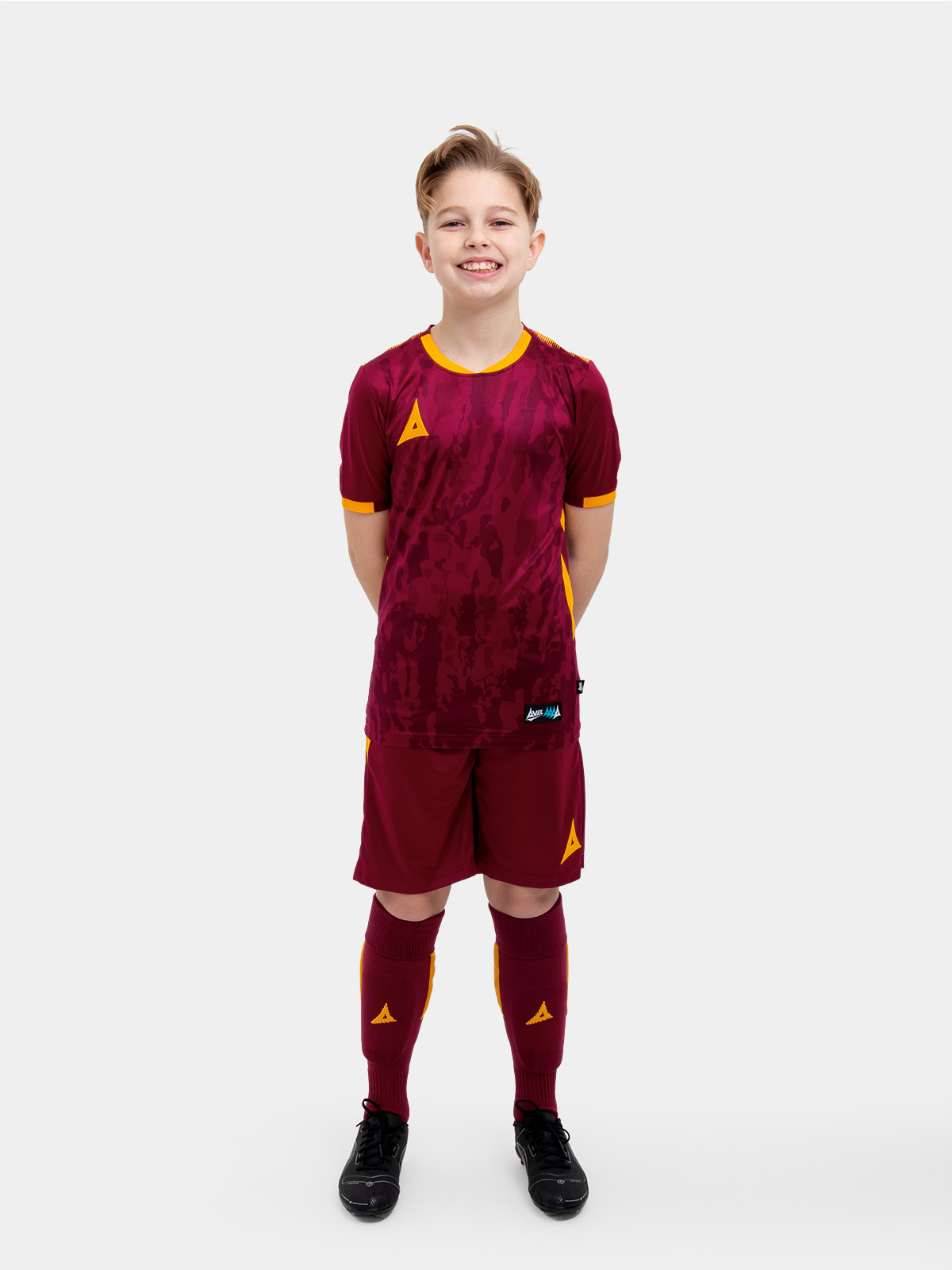 	a child standing up wearing a claret and amber football shirt, shorts and football socks.