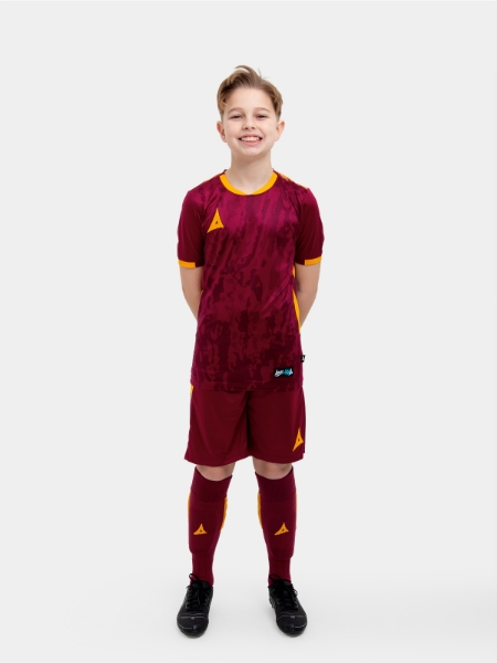 	A child standing up wearing a claret and amber football shirt, Shorts and Football Socks.