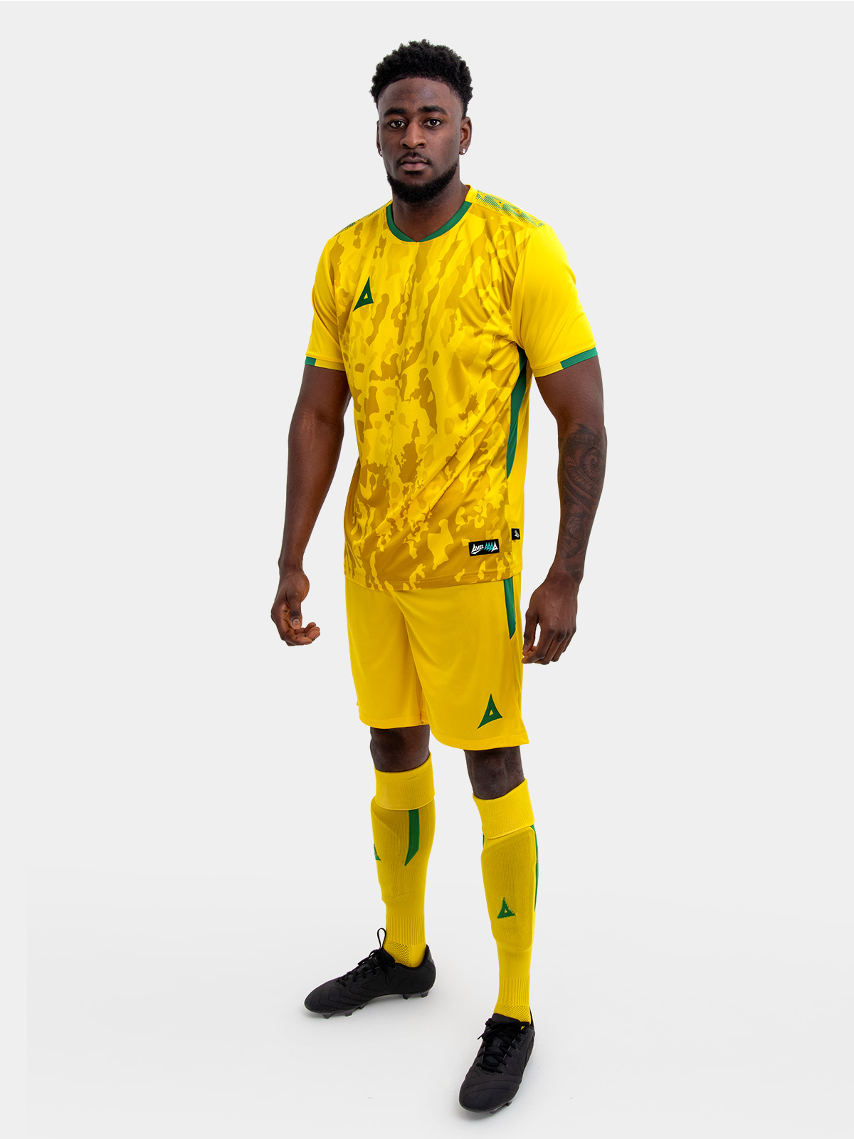 a model standing up wearing a yellow and green football shirt, yellow shorts and yellow football socks.