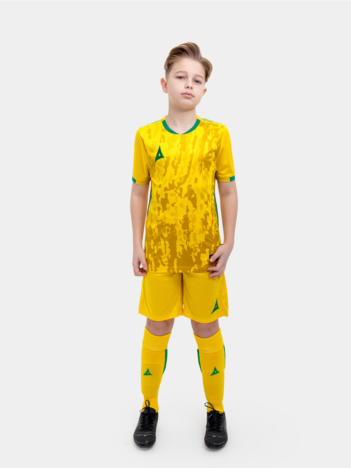 	a child standing up wearing a yellow and green football shirt, yellow shorts and yellow football socks.