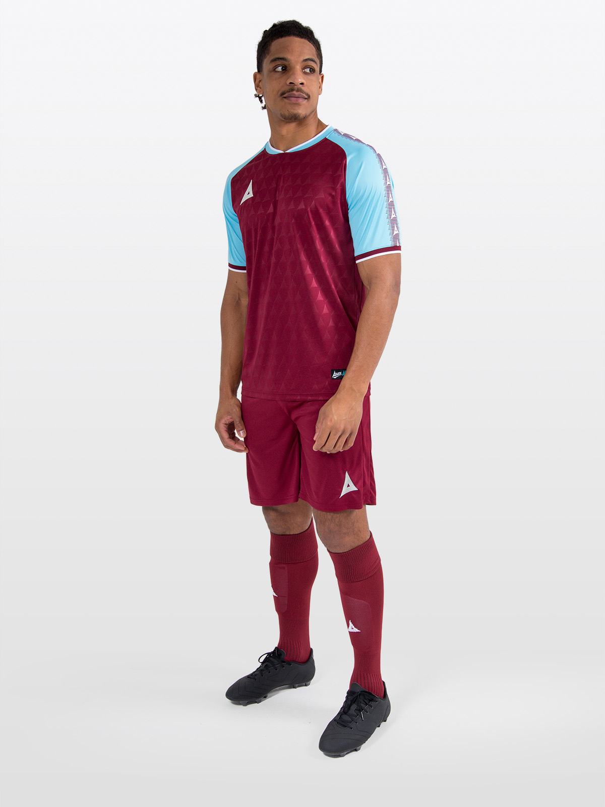 a model standing up wearing a claret / maroon football shirt, matching claret shorts and claret football socks.