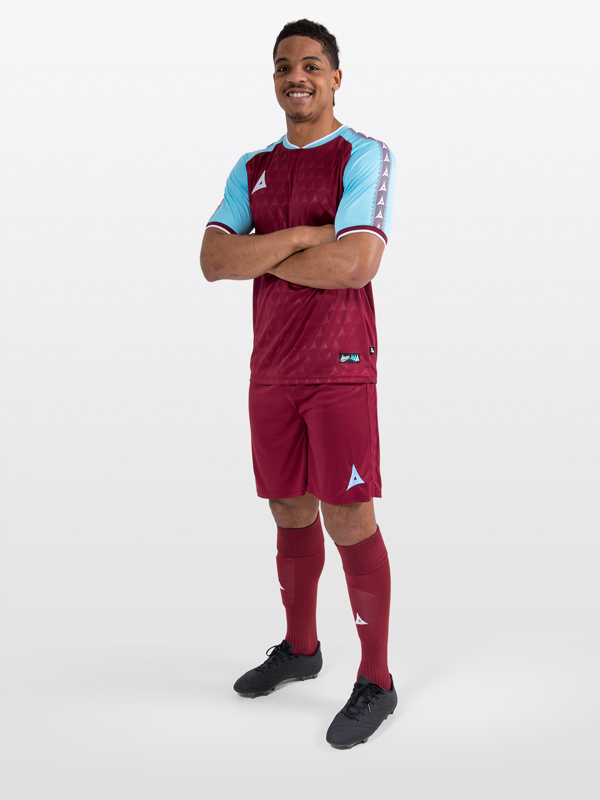a model standing up wearing a claret / maroon football shirt, matching claret shorts and claret football socks.