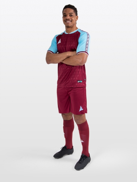 A model standing up wearing a claret / maroon football shirt, matching claret Shorts and claret Football Socks.