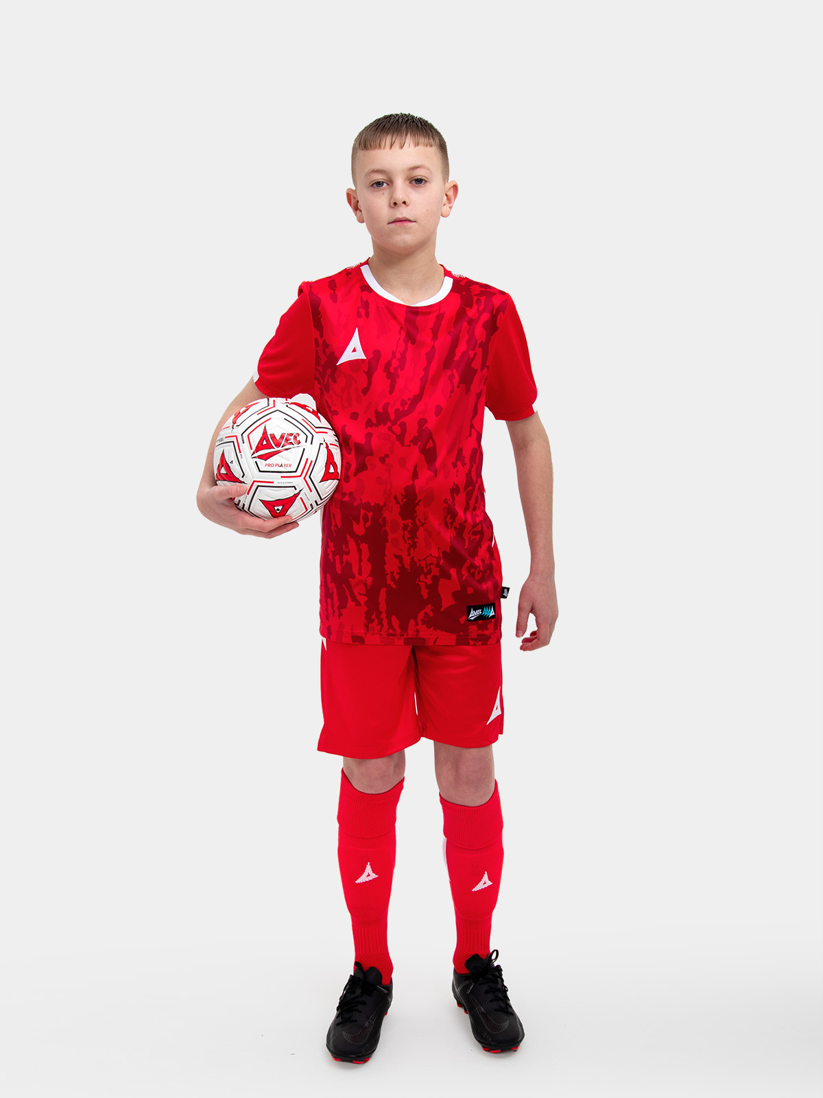 	a young child is wearing a red football shirt. the football shirt has a camo pattern and matching red socks and shorts